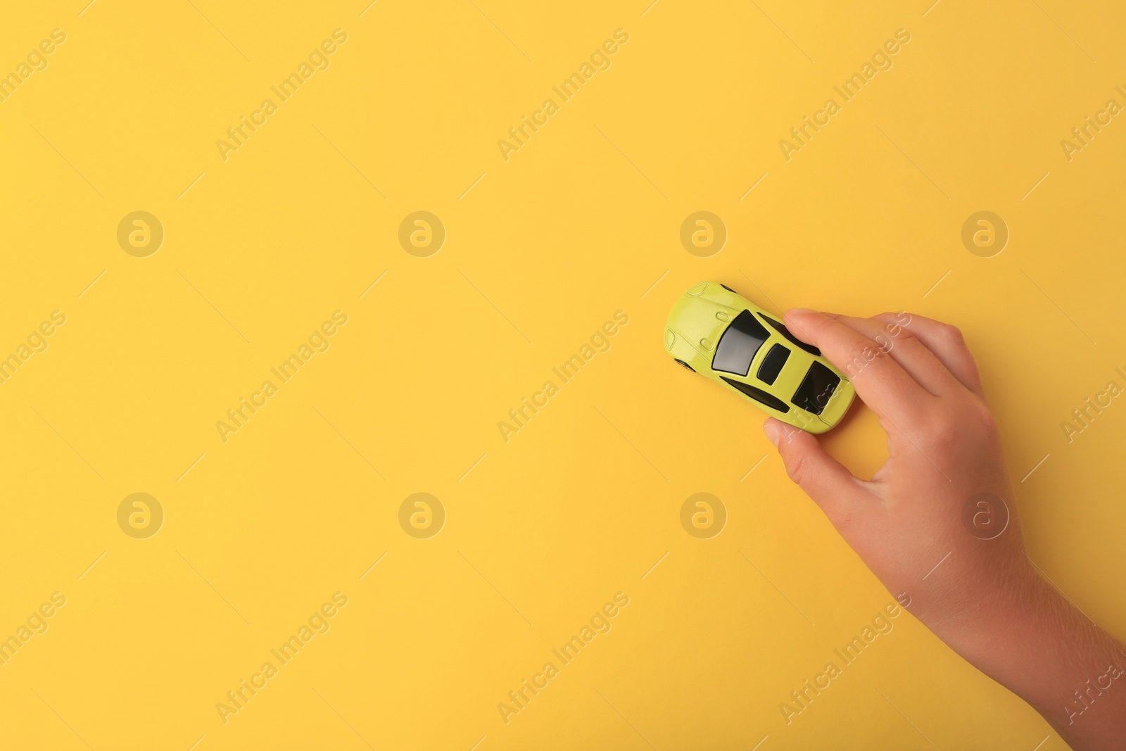 Photo of Child playing with toy car on yellow background, top view. Space for text