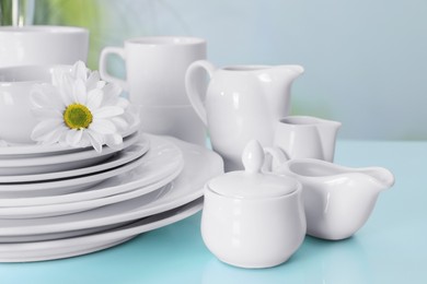 Set of clean dishware and flower on light blue table, closeup