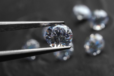 Photo of Tweezers with beautiful shiny diamond above dark gray table, closeup