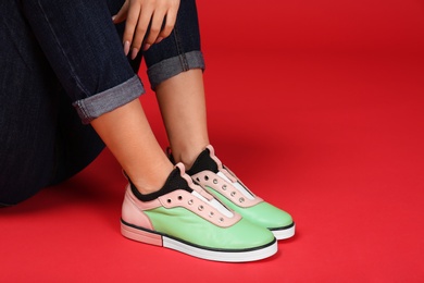 Woman in stylish shoes sitting on color background