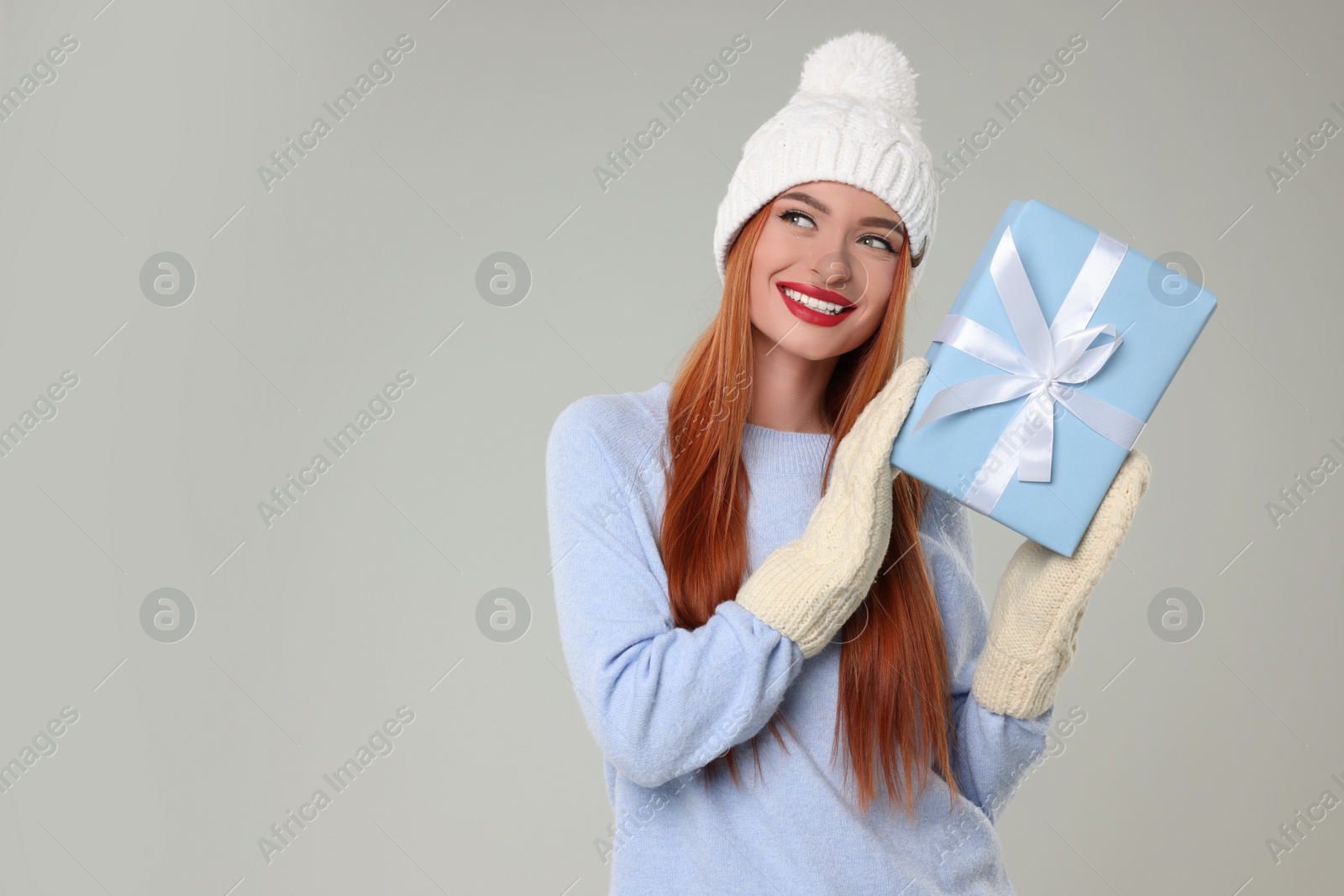 Photo of Young woman in hat and sweater with Christmas gift on light grey background, space for text