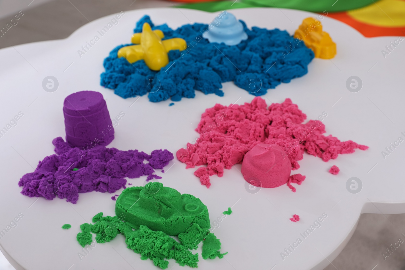 Photo of Bright kinetic sand and toys on white table indoors