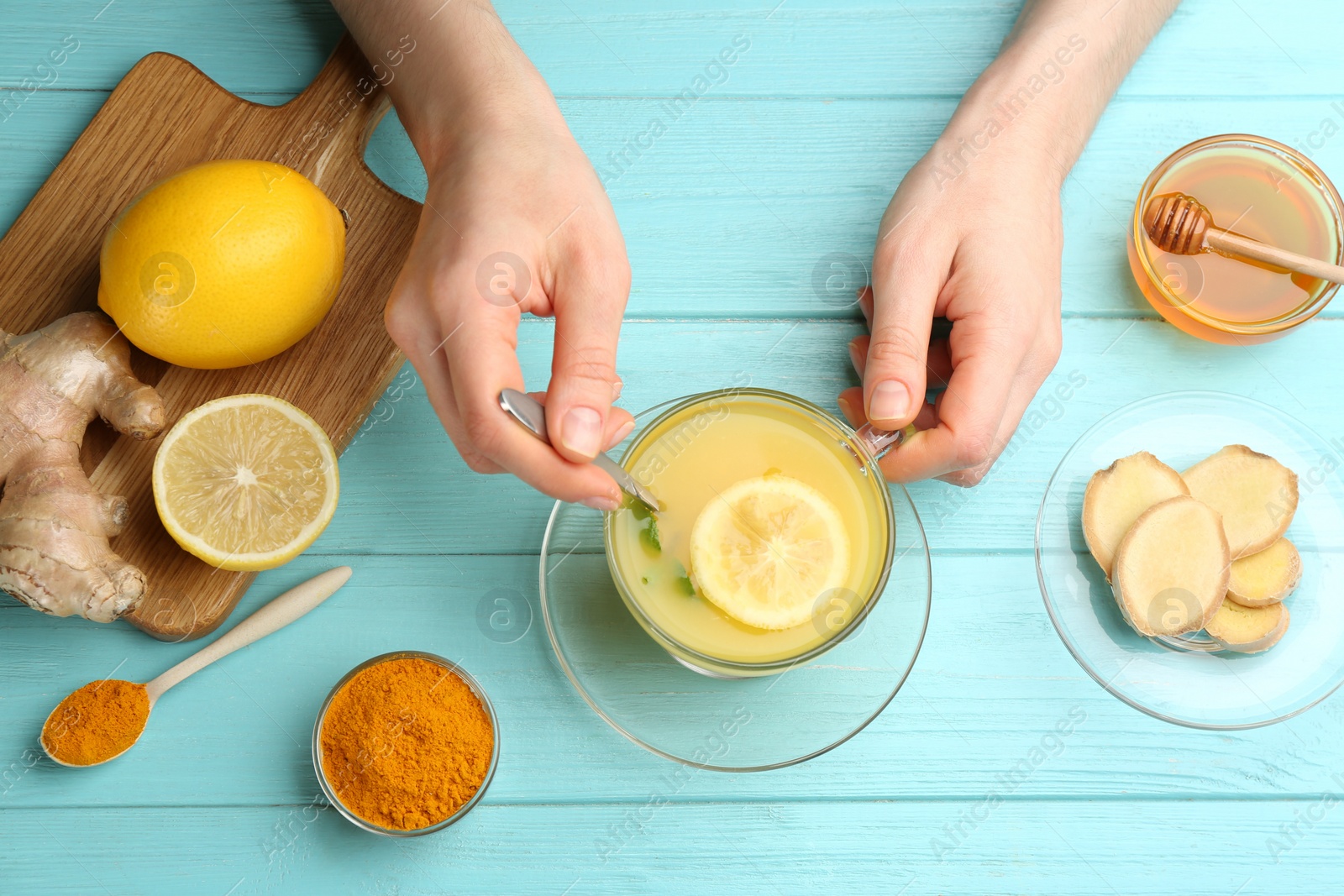 Photo of Woman with cup of immunity boosting drink at turquoise wooden table, top view