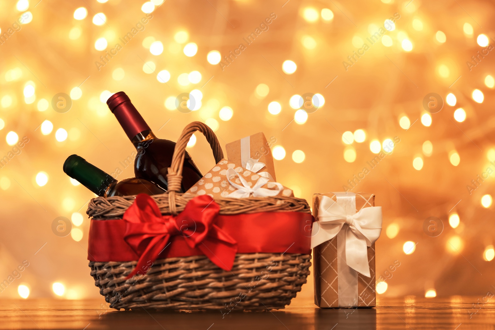 Photo of Gift basket with bottles of wine against blurred lights. Space for text