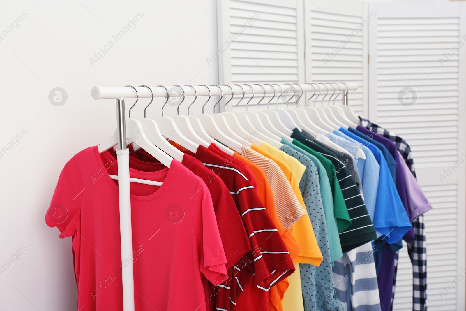 Photo of Rack with bright clothes in room. Rainbow colors