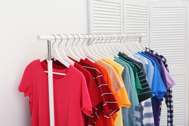 Rack with bright clothes in room. Rainbow colors