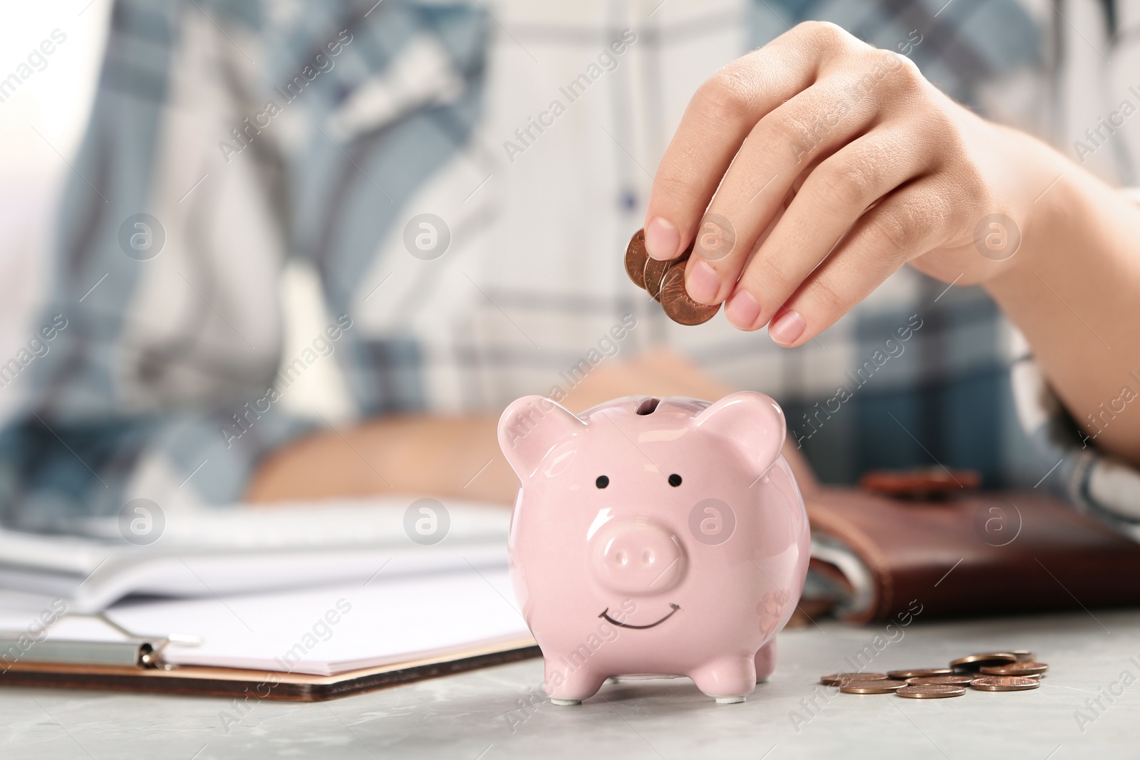 Photo of Woman putting money into piggy bank at table, closeup