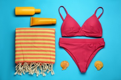 Photo of Beach towel, swimsuit and sun protection products on light blue background, flat lay