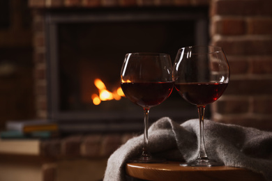 Glasses of red wine on wooden table near fireplace. Space for text