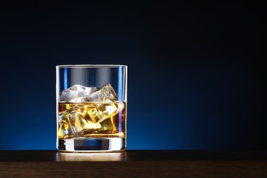 Photo of Whiskey with ice cubes in glass on table. Space for text