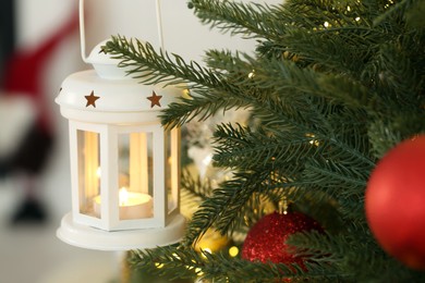 Photo of Christmas lantern with burning candle on fir tree against blurred background, closeup