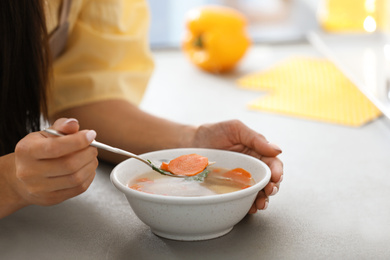 Young woman eating tasty vegetable soup at table, closeup