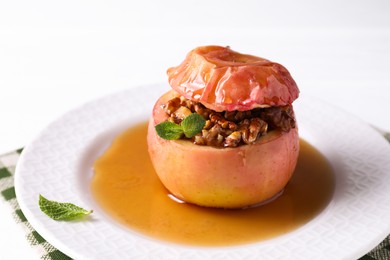 Photo of Tasty baked apple with nuts, honey and mint on white table, closeup