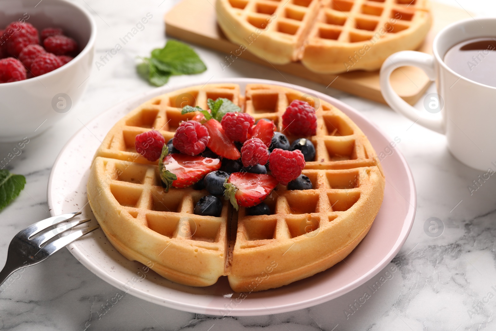 Photo of Tasty Belgian waffles with fresh berries served on white marble table, closeup