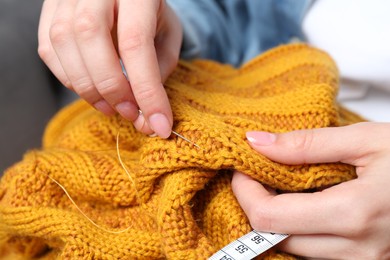 Woman sewing sweater with needle, closeup view