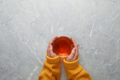 Photo of Woman holding cup of hot tea at grey marble table, top view. Cozy winter