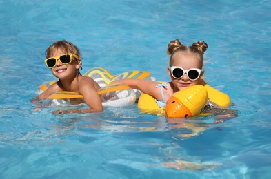 Photo of Happy children with inflatable rings in outdoor swimming pool on sunny summer day