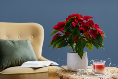 Photo of Beautiful Poinsettia, candles and garland on wooden table indoors, space for text. Interior elements