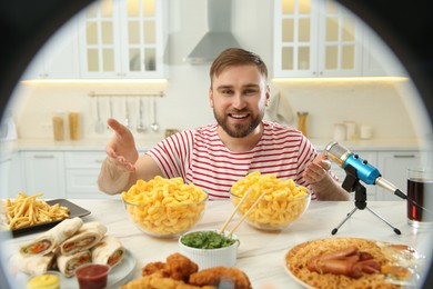 Photo of Blogger with lots of food and microphone at table in kitchen, view through ring light. Mukbang vlog