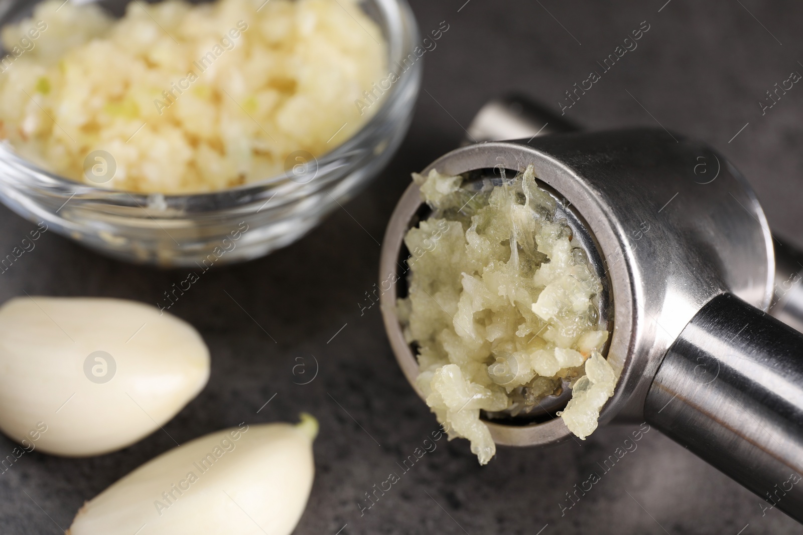 Photo of Garlic press, cloves and mince on grey table, closeup