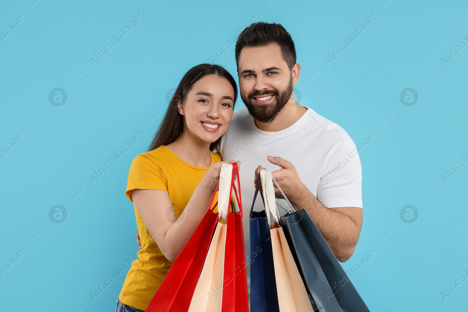 Photo of Happy couple with shopping bags on light blue background