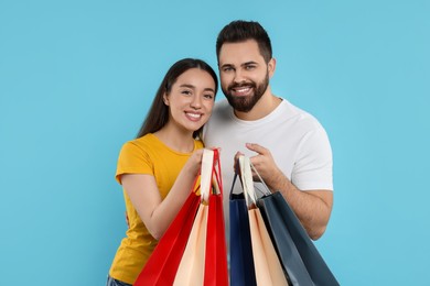 Happy couple with shopping bags on light blue background