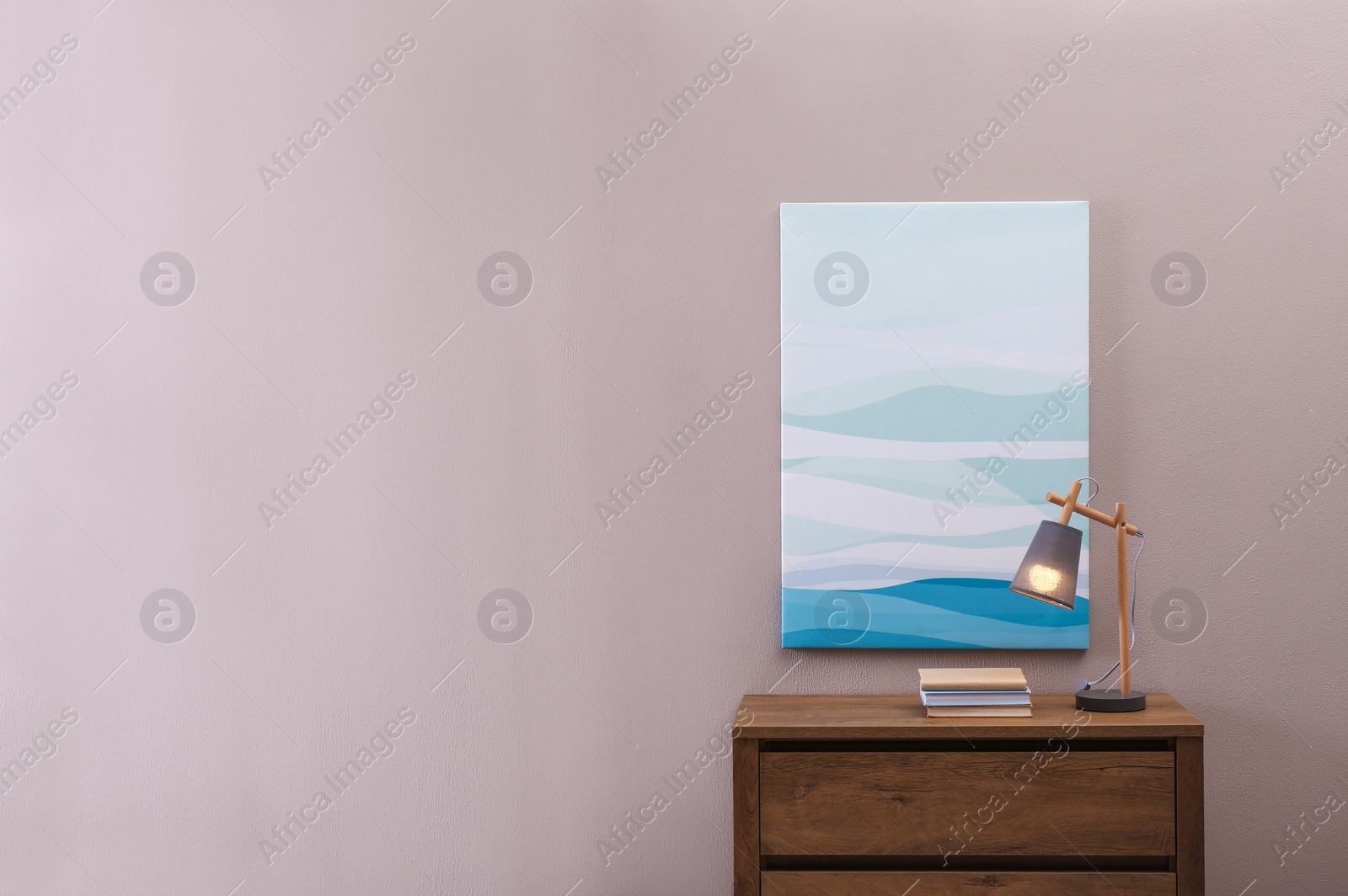 Photo of Wooden chest of drawers with books and lamp near beige wall in room, space for text. Interior design