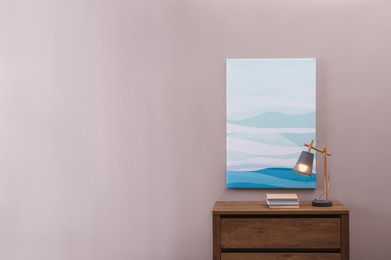 Wooden chest of drawers with books and lamp near beige wall in room, space for text. Interior design