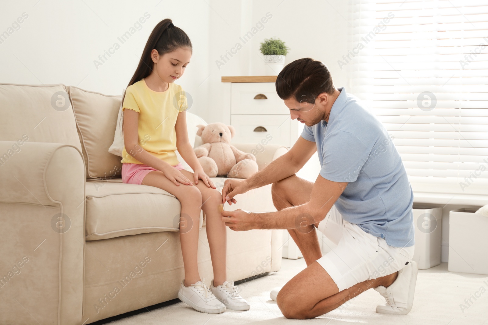 Photo of Father putting sticking plaster onto daughter's leg at home