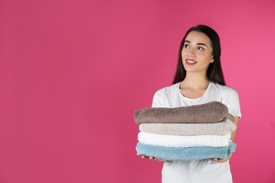 Photo of Happy young woman holding clean towels on color background, space for text. Laundry day