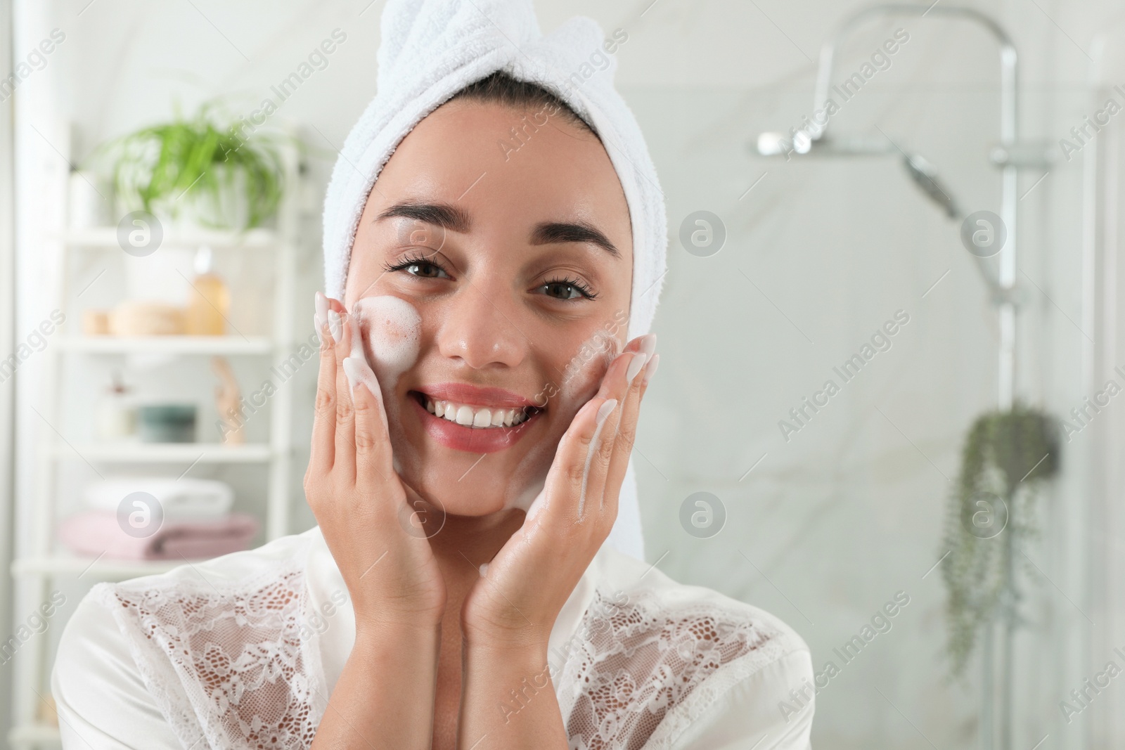 Photo of Beautiful young woman applying cleansing foam onto face in bathroom. Skin care cosmetic