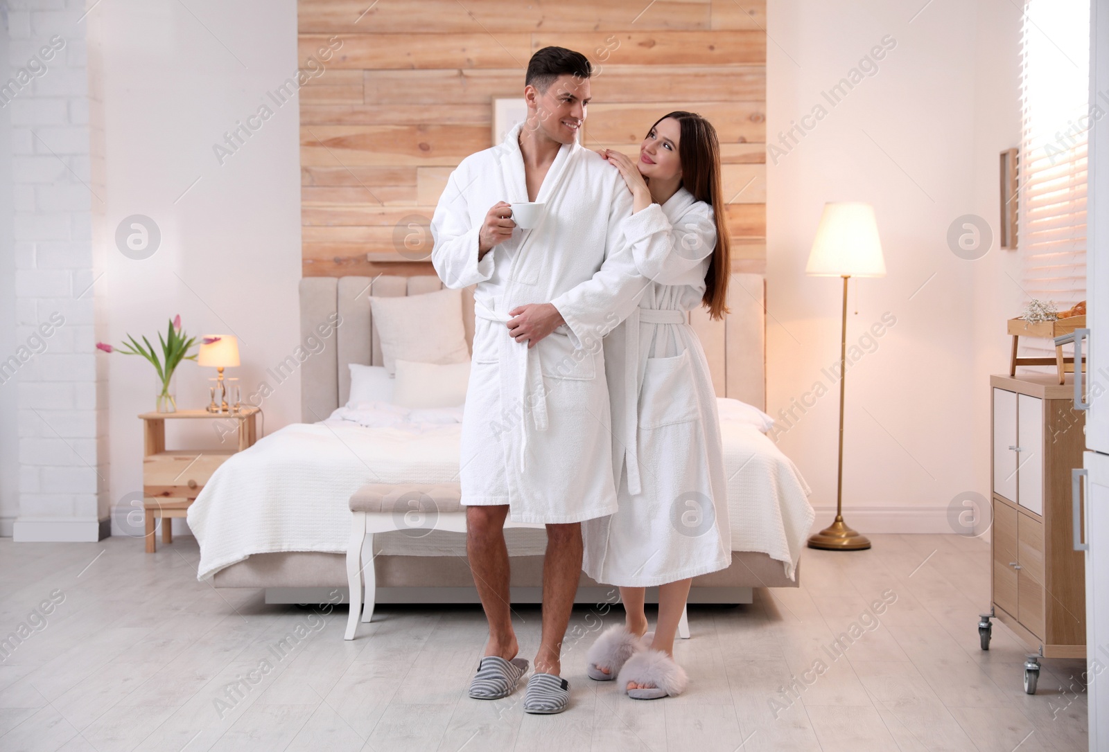 Photo of Happy couple in bathrobes with coffee in bedroom