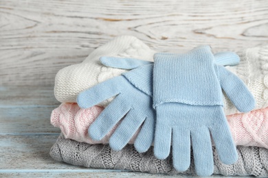 Photo of Stacked sweaters and gloves on wooden table, closeup. Autumn clothes