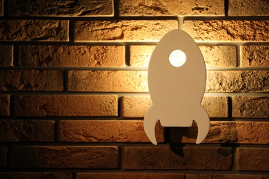 Photo of Rocket shaped night lamp on brick wall. Space for text