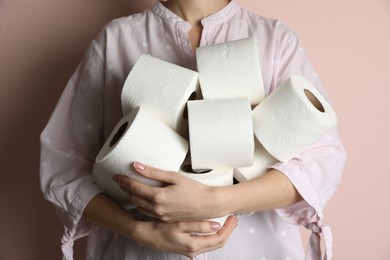 Photo of Woman with heap of toilet paper rolls on pink background, closeup