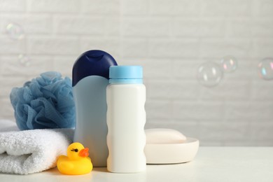 Baby cosmetic products, bath duck, sponge and towel on white table against soap bubbles. Space for text