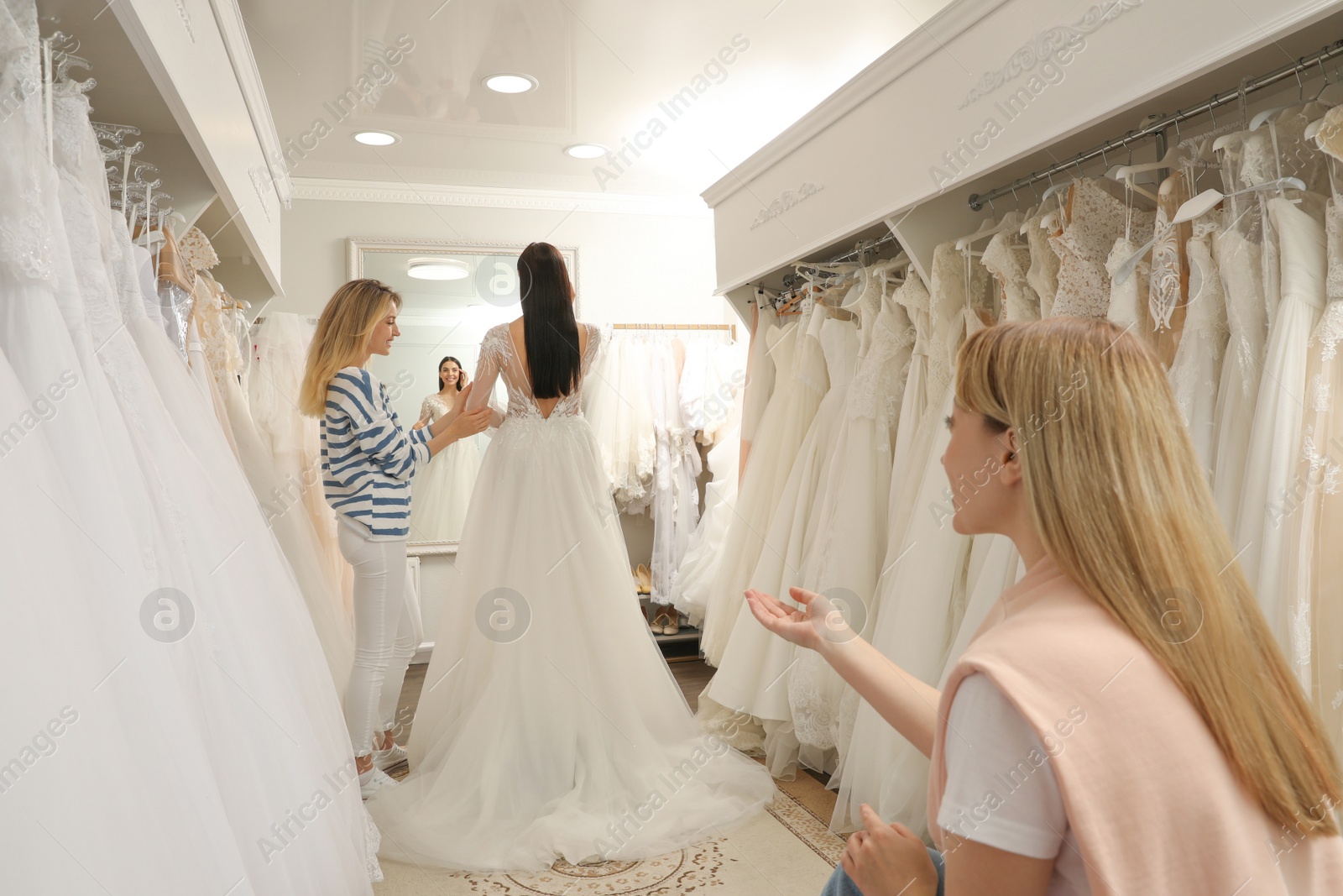 Photo of Bride with friends choosing wedding dress in boutique