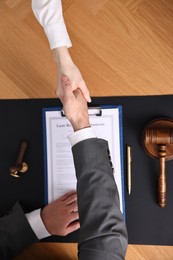 Photo of Notary shaking hands with client at wooden table, top view