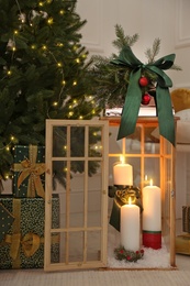 Wooden decorative lantern with burning candles near Christmas tree in room