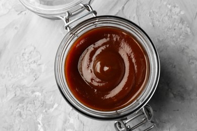 Photo of Tasty barbeque sauce in open jar on grey textured table, top view