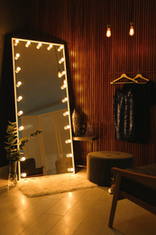 Photo of Stylish large mirror with light bulbs in dark room. Modern interior design