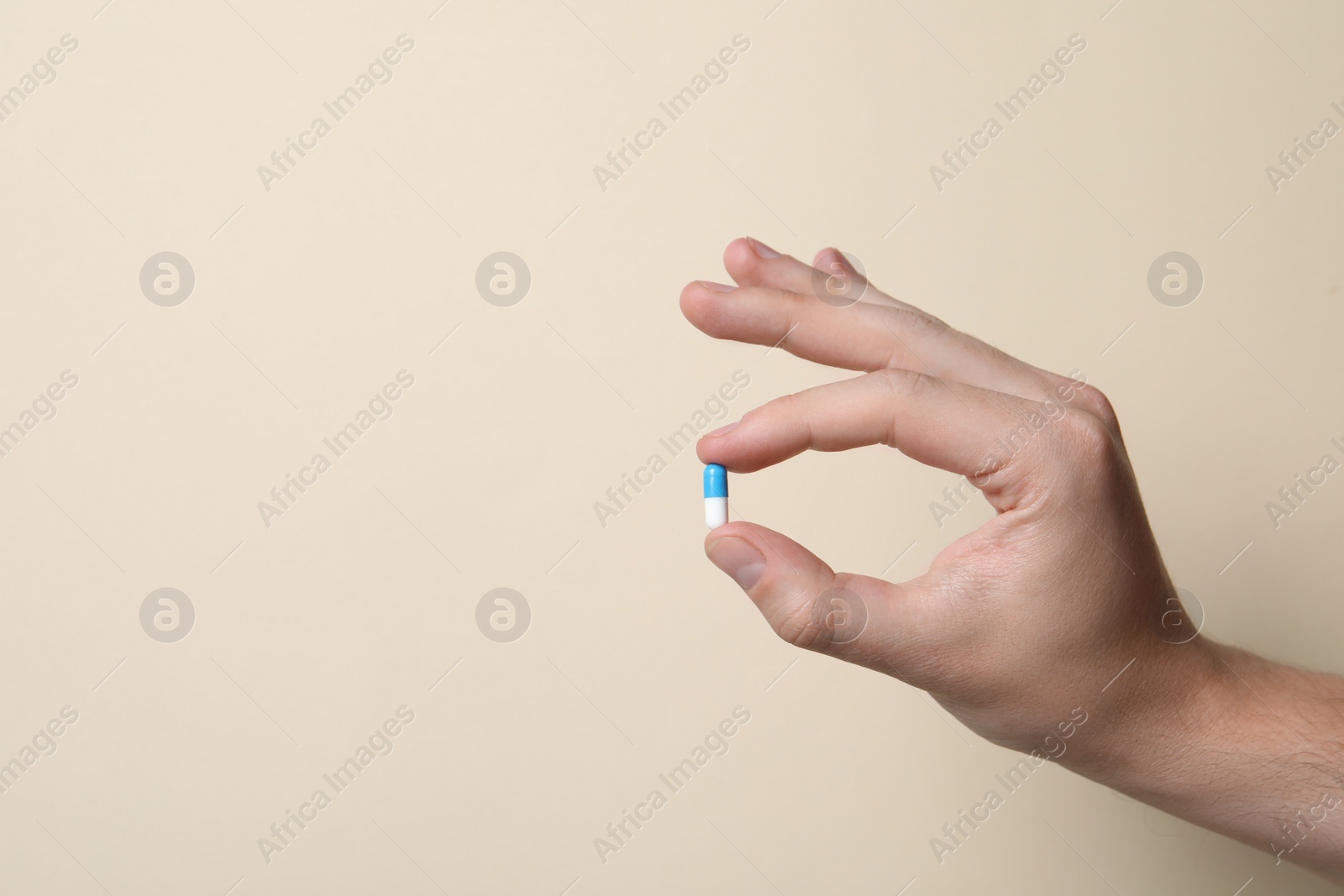 Photo of Man holding pill on beige background, closeup. Space for text