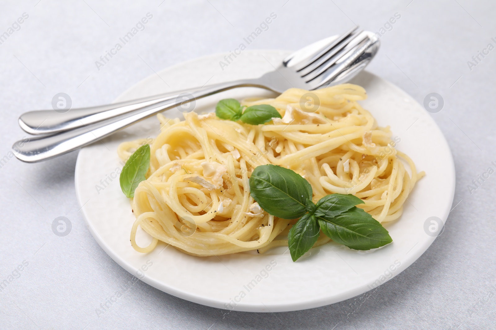 Photo of Delicious pasta with brie cheese and basil leaves on light grey table, closeup