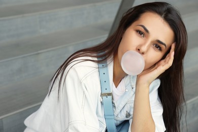 Photo of Stylish woman blowing gum near stairs outdoors