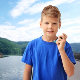 Little boy with asthma inhaler near lake. Emergency first aid during outdoor recreation