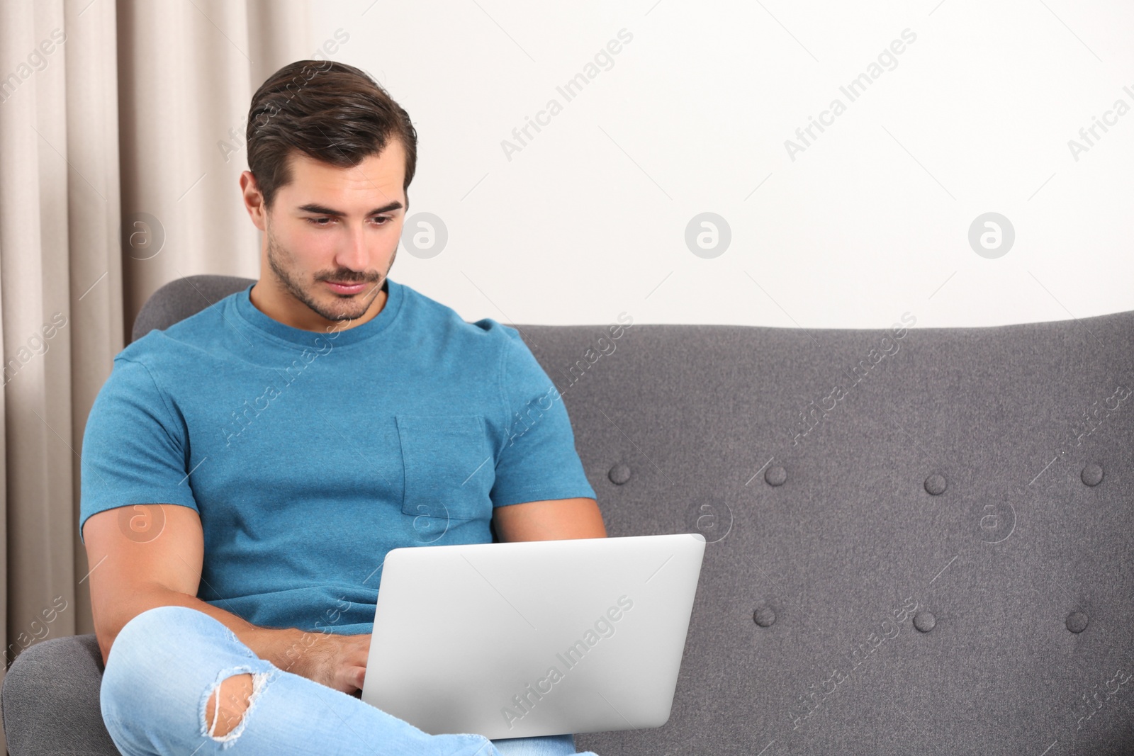Photo of Handsome young man working with laptop on sofa indoors