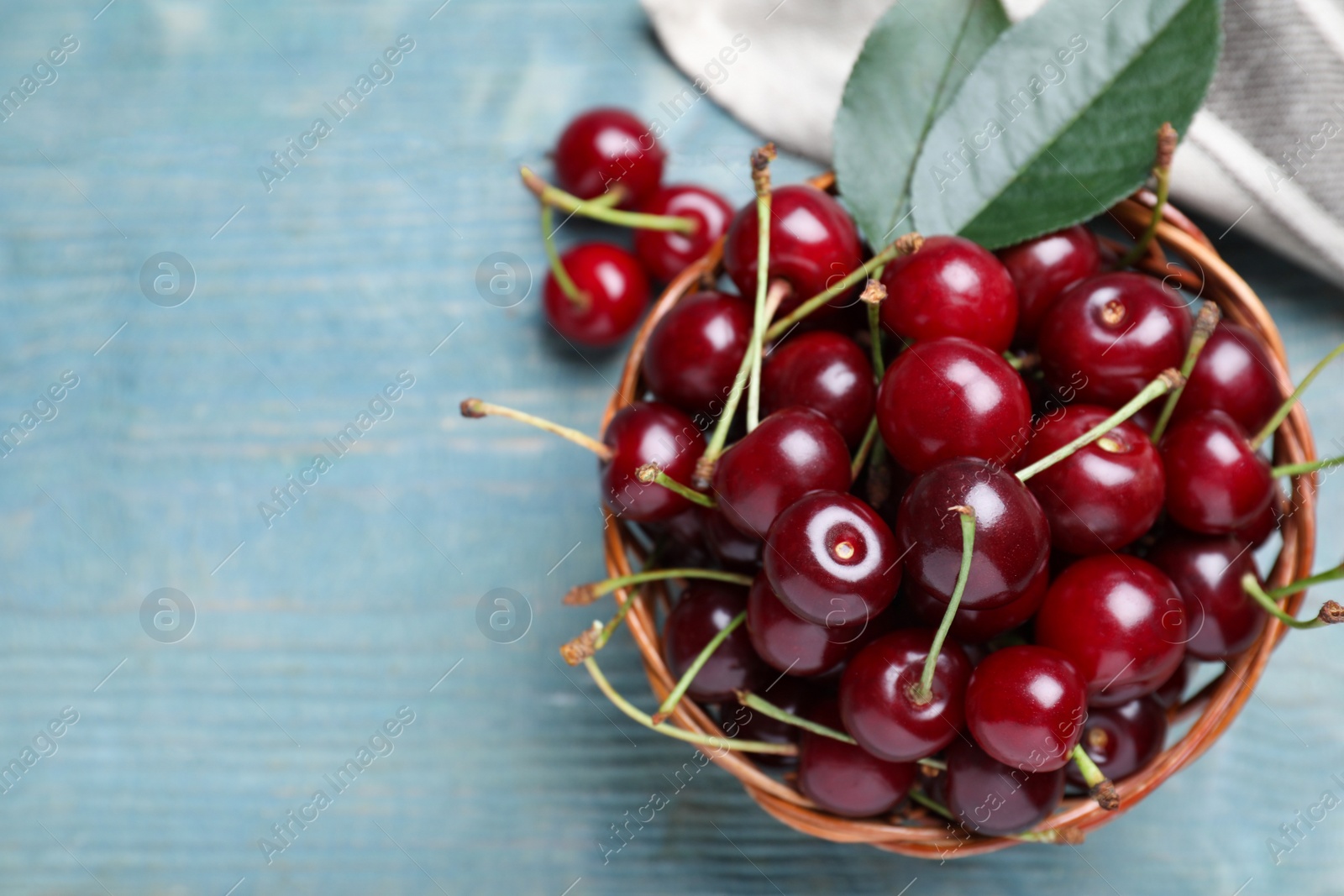 Photo of Sweet juicy cherries with leaves on light blue wooden table, top view. Space for text