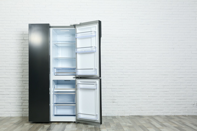 Modern empty refrigerator near white brick wall, space for text