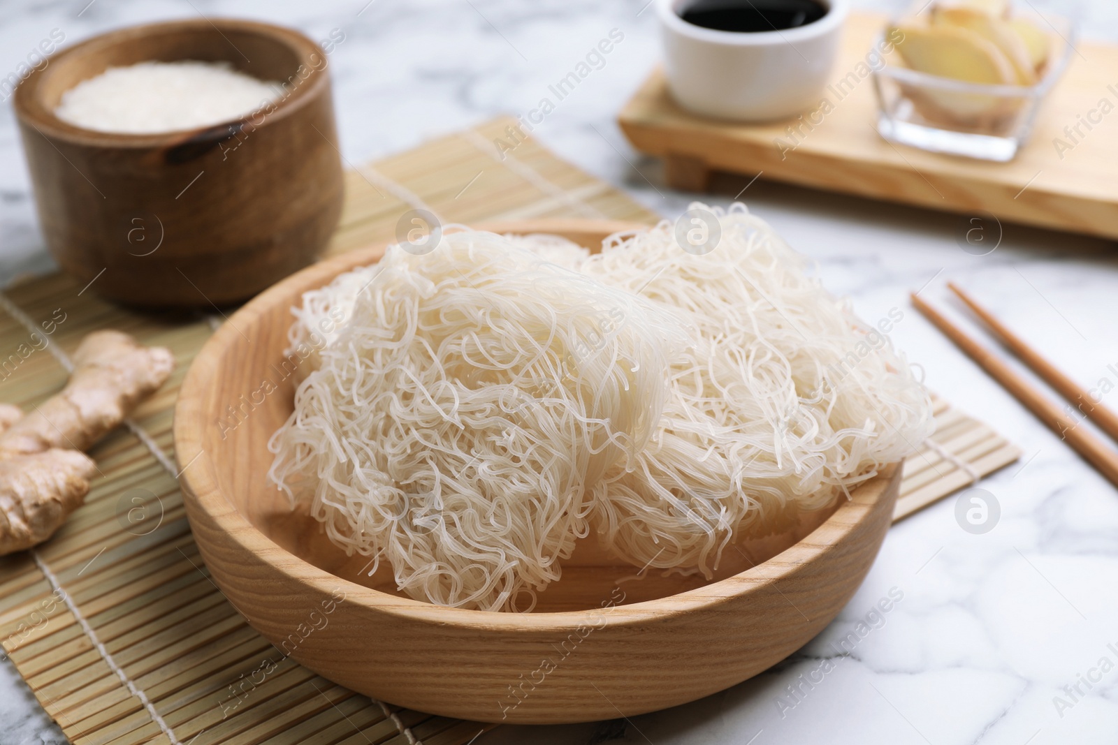 Photo of Bowl with uncooked rice noodles on white marble table