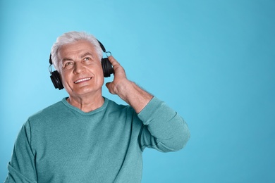 Photo of Mature man enjoying music in headphones on color background. Space for text
